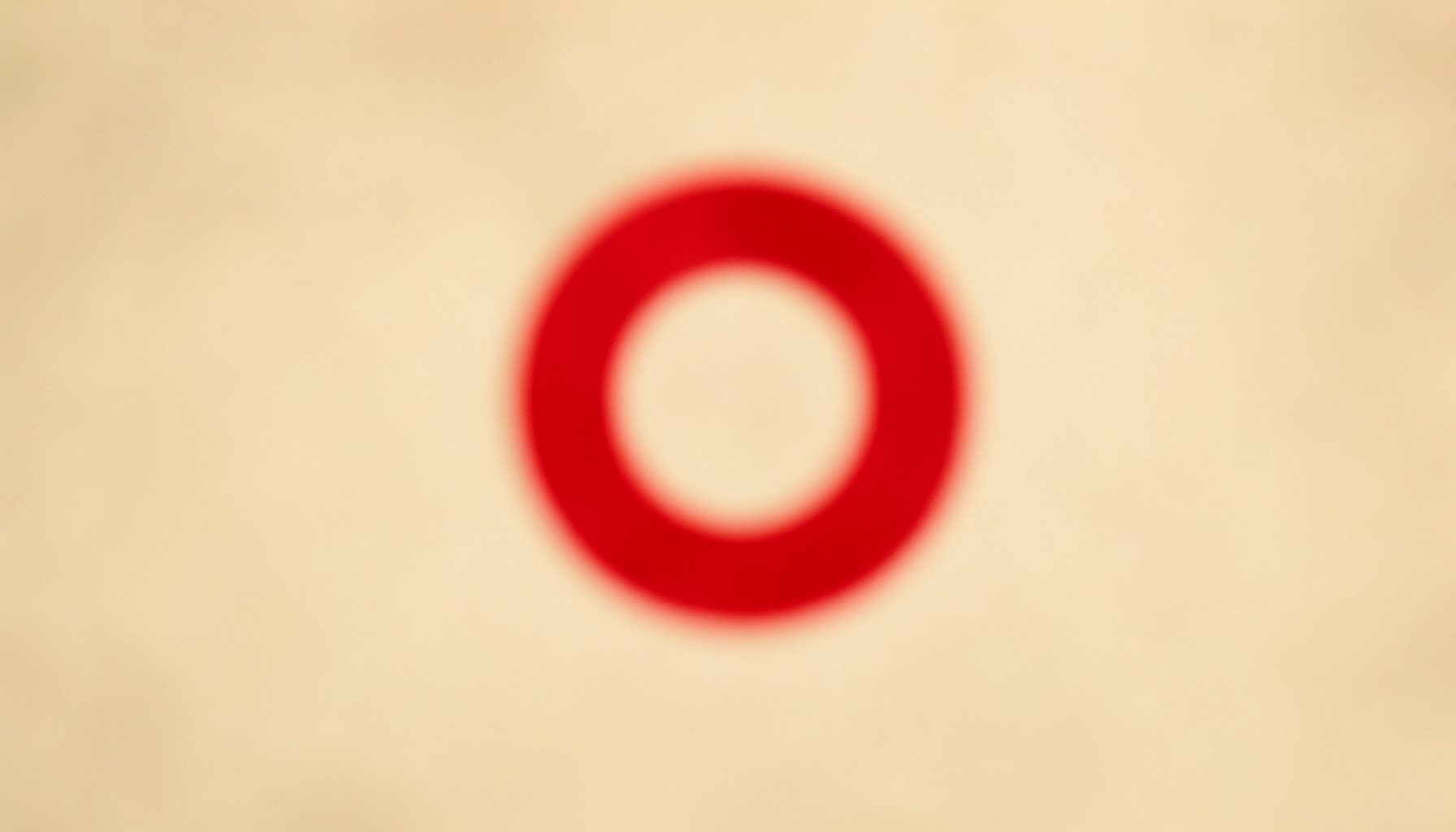 Close-up blurred image of a red ring shape against a soft beige background